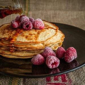 A stack of pancakes with raspberries and syrup